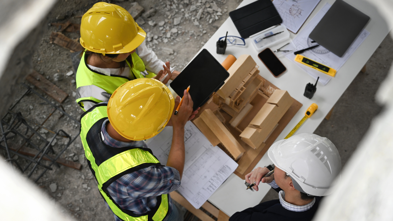 Construction team reviewing blueprints and plans on site with hard hats and safety vests