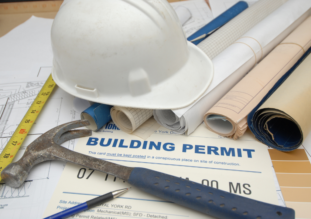 Building permit on top of construction blueprints with a hard hat and tools — permits and inspections for custom home builds in Gulf Shores AL